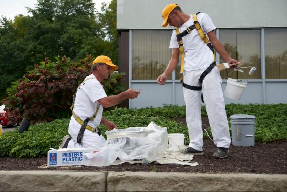  Two commericial painters with harnesses as well as safety and security equipment on prepping for a paint work outdoors